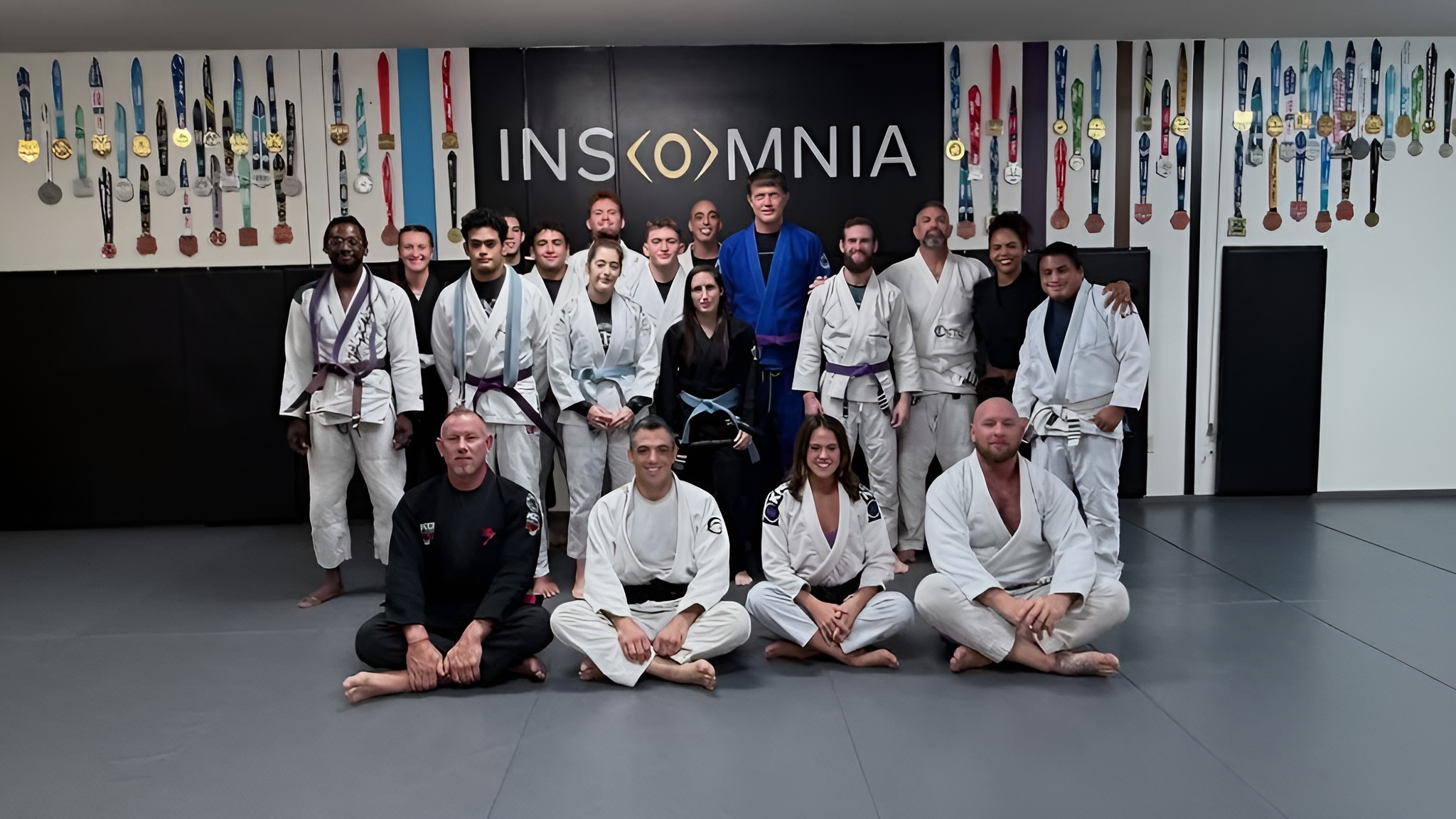 The Insomnia Jiu Jitsu community gathered in front of the medal walls
